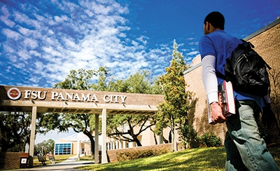 a student wearing a blue shirt walks onto FSU Panama City's campus on a sunny day