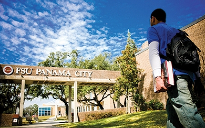 student walking onto FSU Panama City's campus with books in hand
