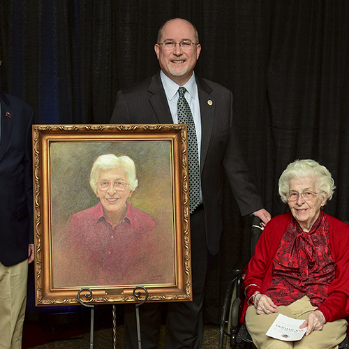 Photo of 2 men and a woman around a painted portrait of the woman